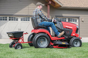 Photo of CRAFTSMAN lawn tractor SKU CMXGZBF7124322 with attached tow-behind spreader, side view on grass.